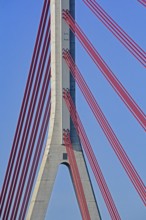Close-up of red cables supporting a concrete pillar of a modern cable-stayed bridge against a