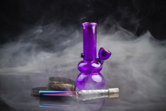 Purple glass bong pipe with joint and a lot of smoke. Cannabis smoker starter pack