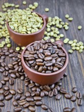 Grains of green and black coffee in brown clay cups and on a table on the background of a wooden
