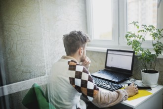 Person with mask sitting at a desk, focused on work on a laptop