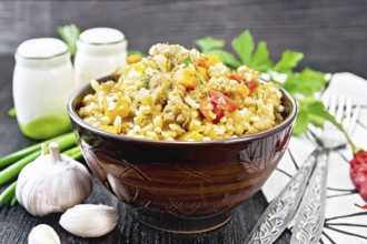 Barley porridge with minced meat, yellow and red bell peppers, garlic and onions in a clay bowl, a
