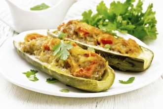 Cucumbers stuffed with minced meat, tomatoes, pepper with cheese and parsley in a plate, cream and