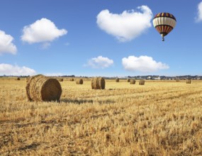 Red and blue balloon slowly floating over kibbutz field. Stacks of harvested wheat beautifully and