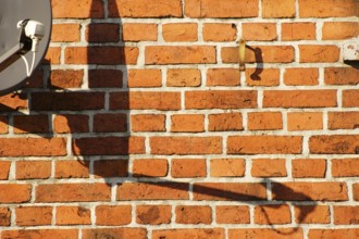 A satellite dish on a brick building casts a shadow