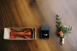 Accessories for the groom bow tie, gold wedding ring and boutonniere on a wooden floor in a row.