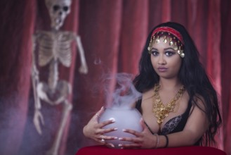 A fortune teller with an oriental look next to a skeleton and a fog vessel, studio shot, staged