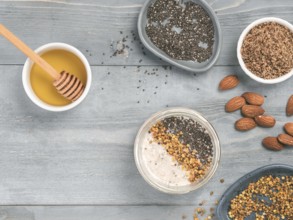 Overnight oats in jar and ingredients - chia seeds, almond, LSA, honey and pollen on gray wooden