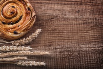 Rich raisin bun bunch of wheat ears on oak wooden board food and drink concept