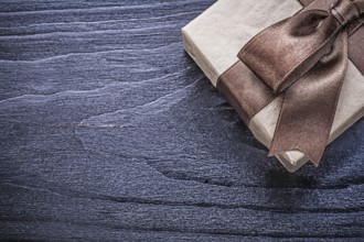 Gift box with brown satin bow on wooden board