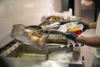 Someone is deep frying food in a professional kitchen with a fryer and metal basket