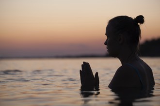 Woman in sea water at sunset alone. She praying or meditating