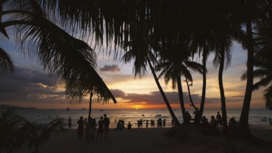 Silhouetted people and palms near sea. Sunset at tropical White beach, Boracay island, Philippines