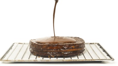 Closeup of chocolate icing pouring over Sacher torte towards white