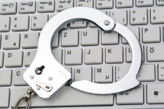 Handcuffs lying on the keyboard of a computer. Symbolic photo for criminality, computer crime and