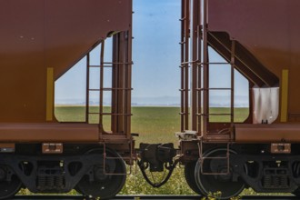 Close up of train coupler connecting two red wagons of a Canadian freight or cargo train. Green
