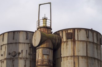 Large rusty industrial tanks and pipes dominate the scene, hinting at a past era of manufacturing
