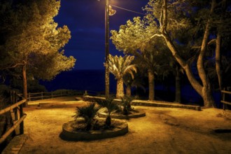 Gloomy square in abandonded park by the sea at midnight illuminated by single lamp, Costa Brava in