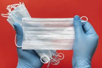 Doctor holds lot respiratory surgical face mask in hands blue medical gloves on red background.