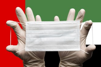 Medic holds protective respiratory face mask in two hands in white gloves on background of national