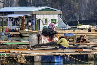 Fishermen work on a floating platform in front of a house on calm waters surrounded by steep