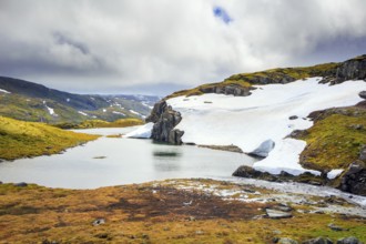 The cold water of the lake is covered with ice floes. Gorgeous Snow Road in Norway. Cold July in