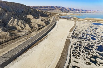 Asphalt highway runs along the sea coast. The picturesque Dead Sea is covered with patterns of salt