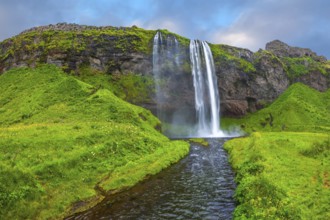 The warm July day in Iceland. Seljalandsfoss waterfall. Rainbow decorates drop of water
