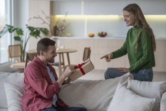 Happy couple celebration. Loving pleased woman gives gift with red tape to smiling husband.