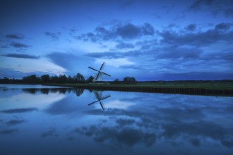 Dutch windmill and clouds in dusk reflected in river, Holland