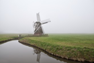 Dutch wooden windmill in fog by canal