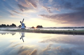 Golden sunrise over windmill reflected in river, Netherlands