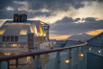 Illuminated AIDA Logo attached to AIDA Bella ship with fence and boat deck in front in the evening
