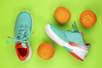 Red, cyan, white pair of new tennis shoes in studio shot over green background with oranges next to