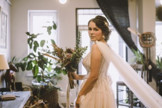 Stylish bride posing at window in light on background. rustic wedding concept. happy bohemian