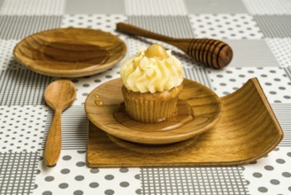 Cupcake and natural honey in a wooden plate with wooden spoon and wooden honey dipper stick