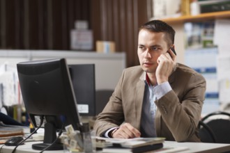 Businessman sitting behind his desk in the office talking on a mobile phone listening to the