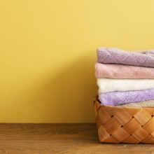 Stack of bath towels in basket on wooden table. yellow background. copy space