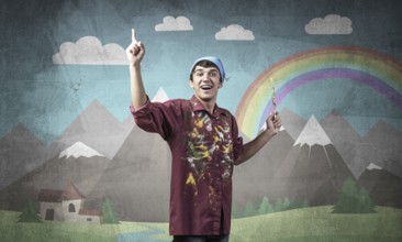 Young male artist with paintbrush. Happy painter in shirt and bandana standing on background