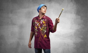 Young emotional artist gesturing with paintbrush. Caucasian painter in dirty shirt and bandana