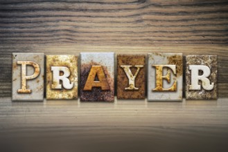 The word PRAYER written in rusty metal letterpress type sitting on a wooden ledge background