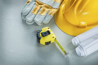 Set of blueprints building helmet protective gloves measuring tape on concrete background