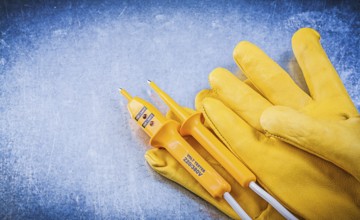 Yellow electrical tester protective gloves on metallic background electricity concept