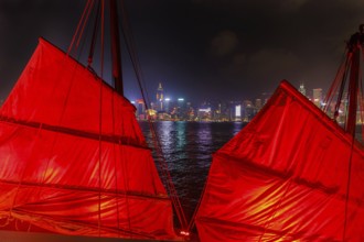 Close up of red-sail junk boat with Hong Kong island skyline background seen from the waterfront of