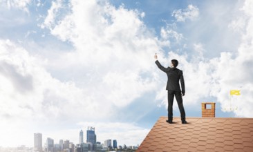 Businessman on house roof touch empty space. Mixed media