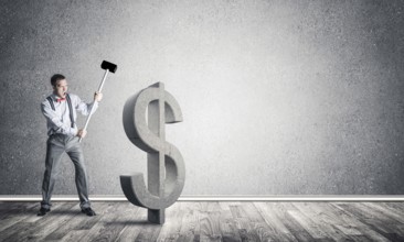 Young furious businessman going to crash with hammer stone dollar symbol