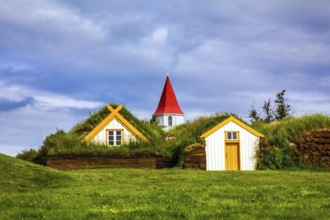 Church bell tower with red gabled roof. The old village of houses covered with turf and grass.