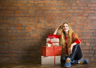 Young woman with Christmas gift near brick wall