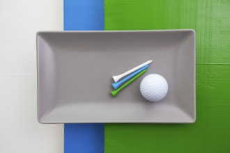Gray ceramic dish with golf equipments on over white, blue and green wooden table, rectangle dish