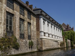Historic buildings with brick façade along a canal, partly surrounded by greenery, under a clear