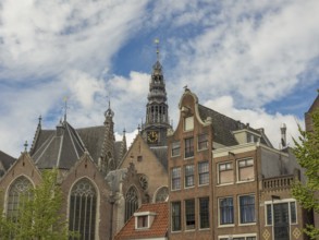 A church with a distinctive clock tower towers over historic buildings under a partly cloudy sky,